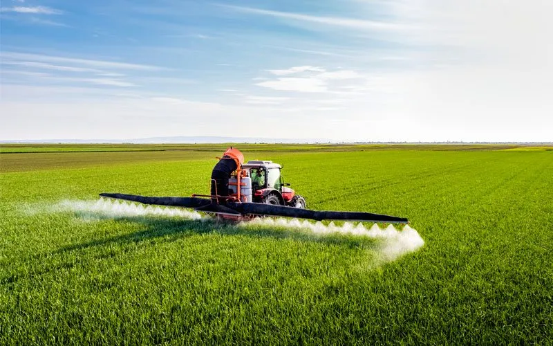 Tractor with boom sprayer applying agrochemicals in a field