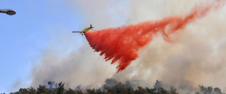 Firefighting aircraft dropping red fire retardant over a forest